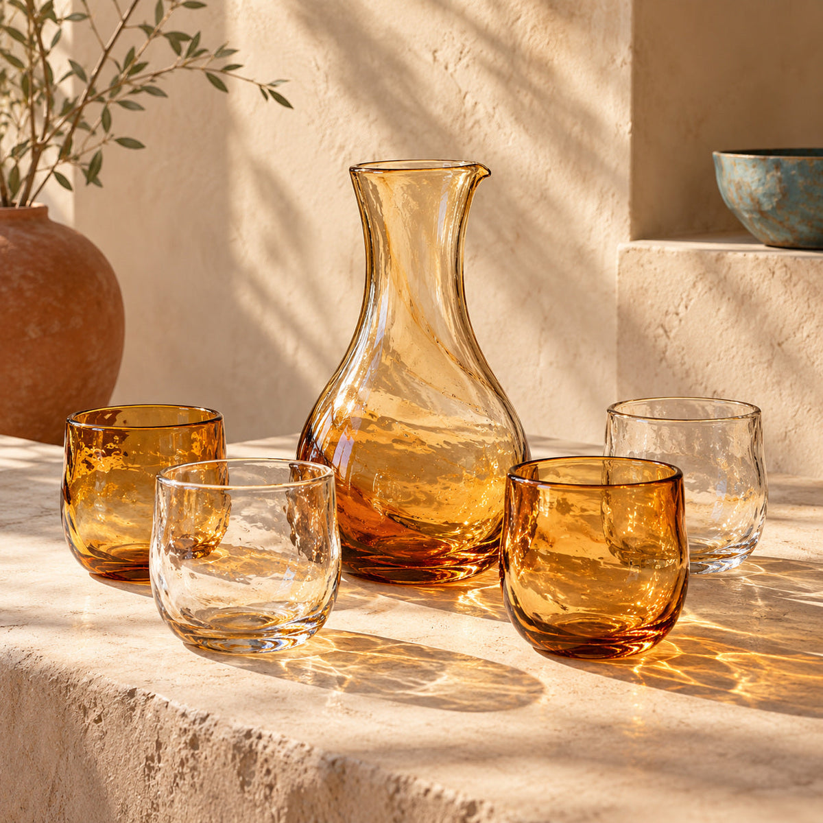 Amber and clear handblown tumblers and a carafe casting warm reflections on plaster.