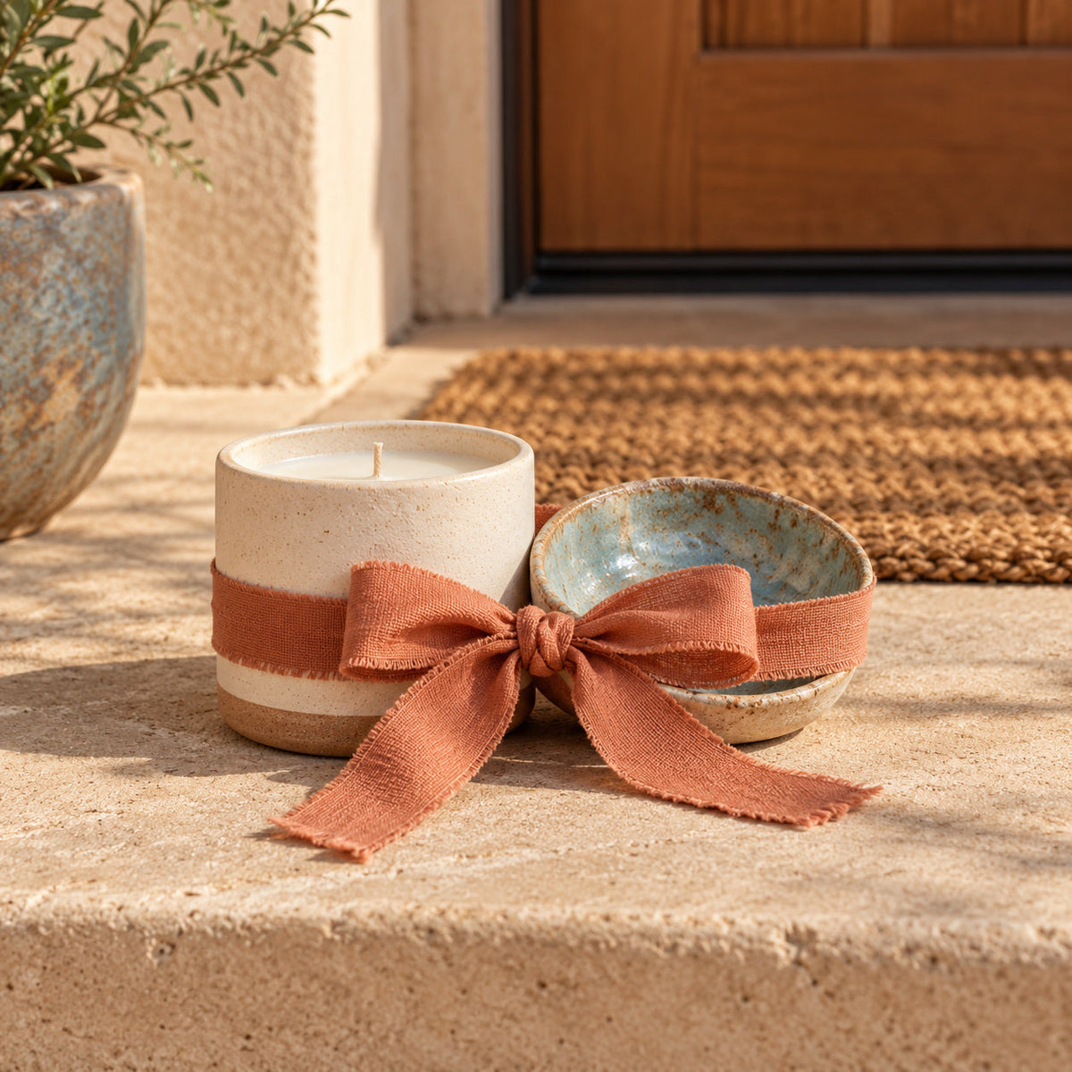 Clay candle and small ceramic dish tied with ribbon near a front-door mat.
