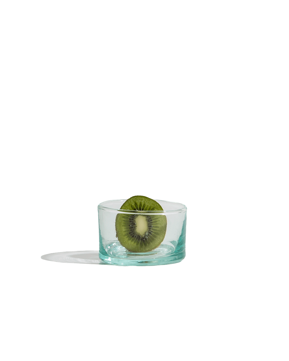 Small hand-blown recycled glass tumbler with a kiwi slice inside, isolated on a deep green ground