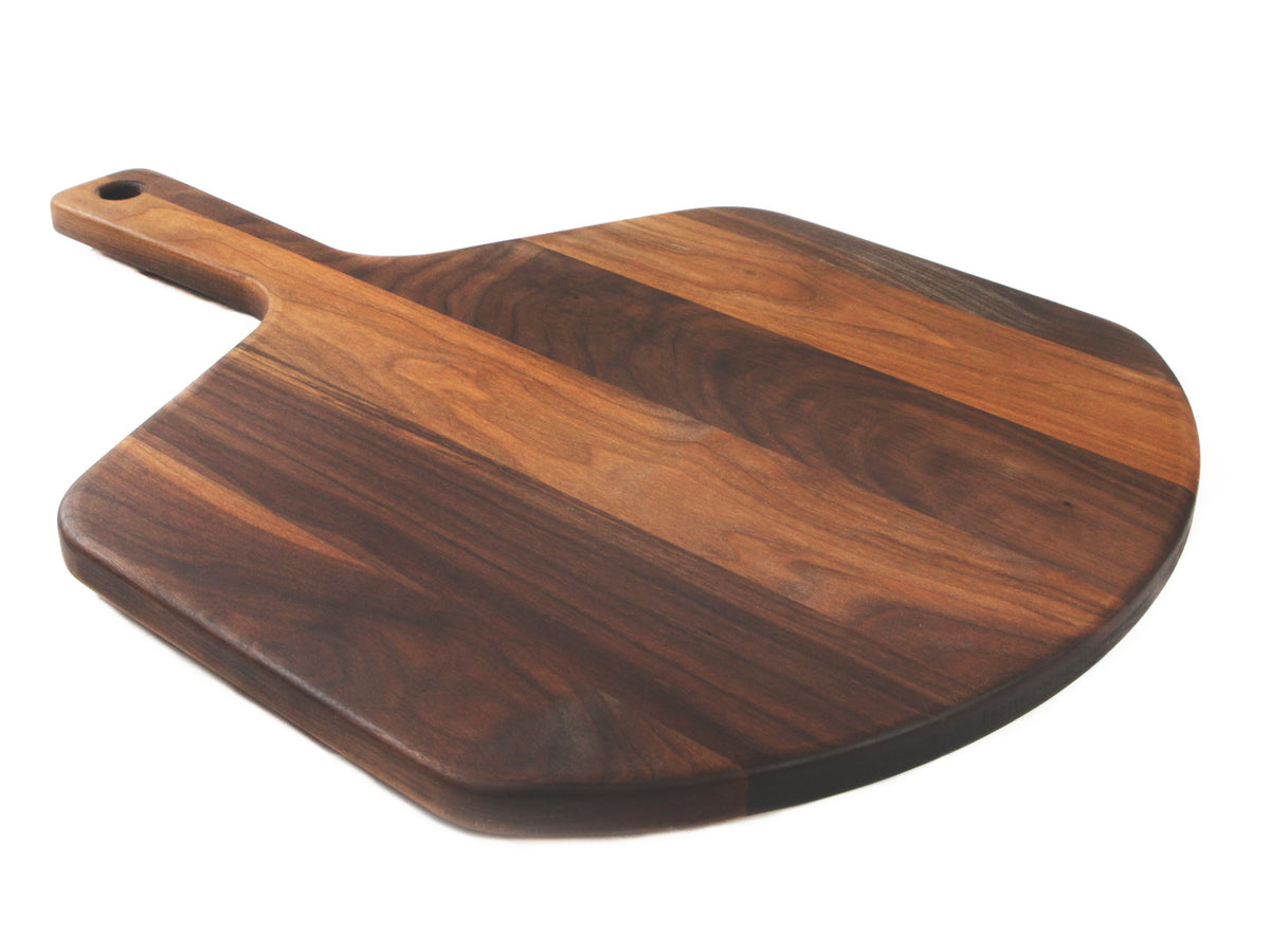 Walnut pizza peel lying at an angle on white, showing the striped grain and short handle