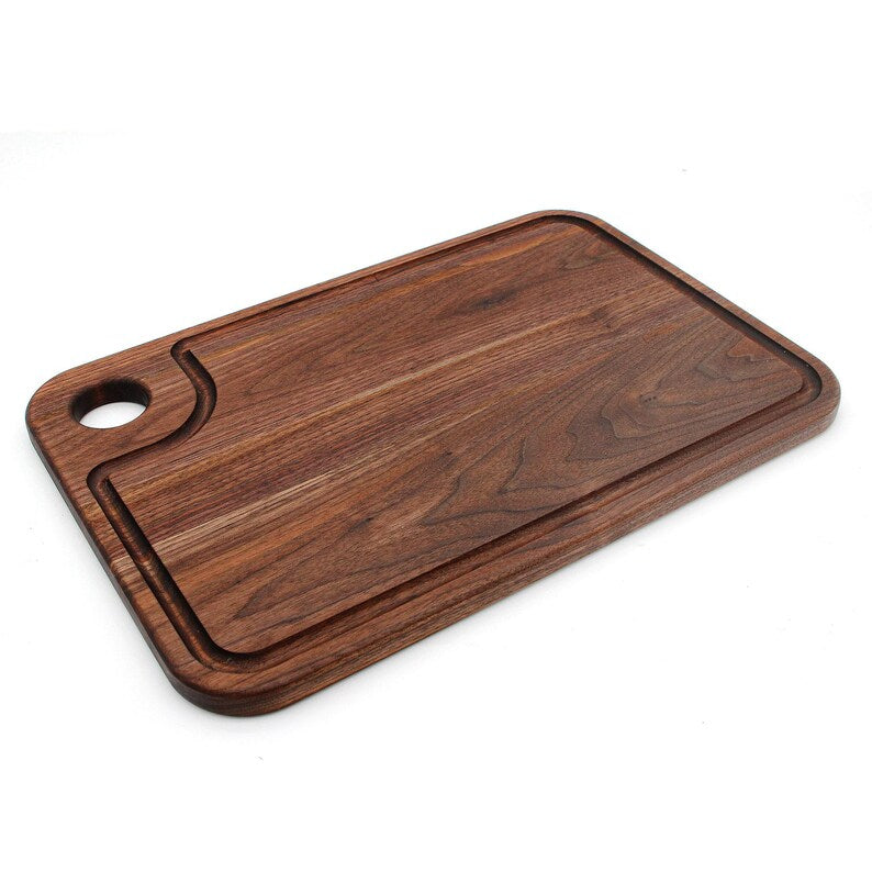 Walnut cutting board with thumb hole and juice groove lying at an angle on white