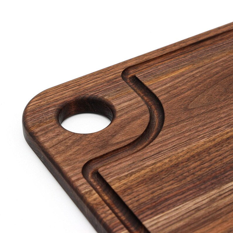 Close-up of the thumb hole corner on a walnut cutting board showing the curved juice groove
