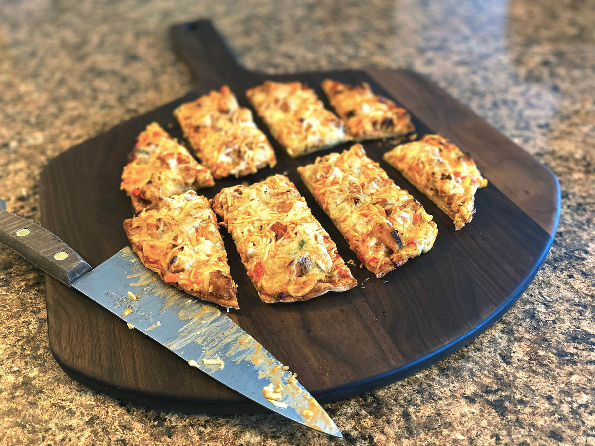 Sliced pizza cut into squares on a walnut pizza peel with a knife on a granite counter
