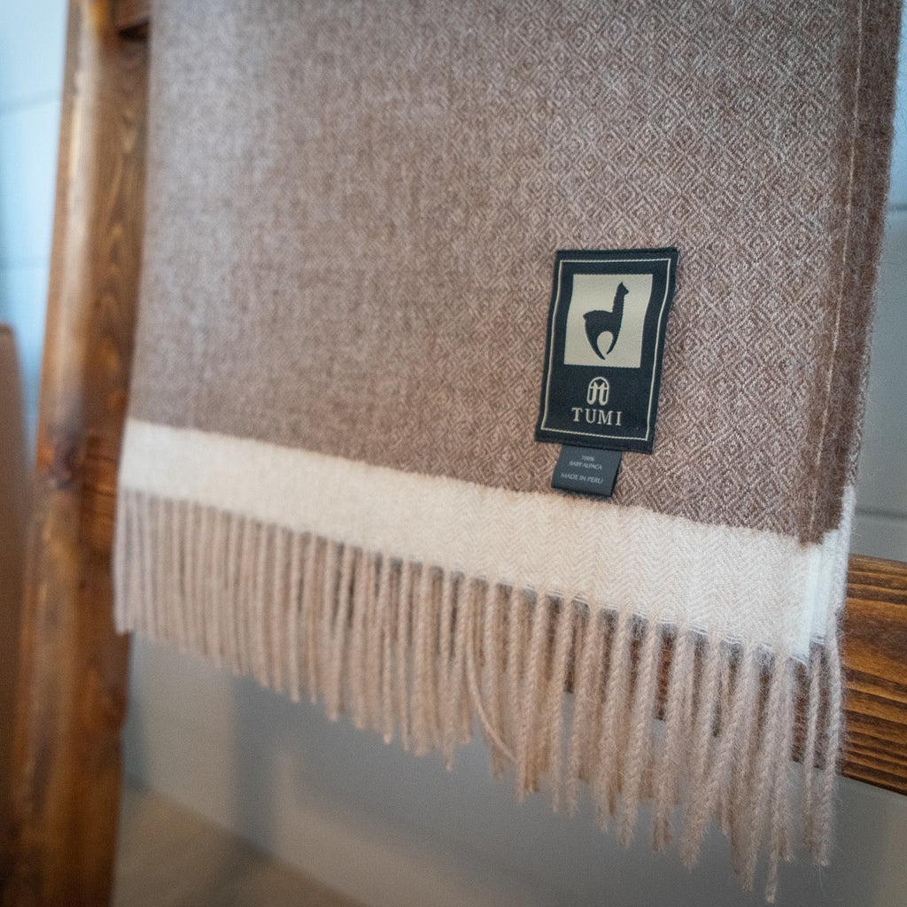 Close view of brown herringbone baby alpaca throw with cream band and long fringe on a wooden ladder