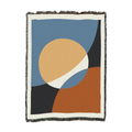 Woven cotton throw with a sand sun over clay and charcoal hills on slate blue, shown flat with fringed edges