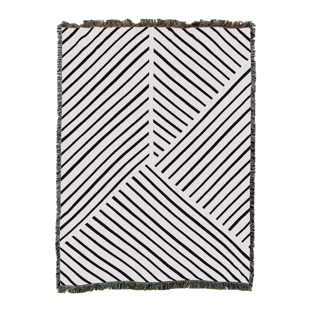 Woven blanket in white with black diagonal line panels meeting at angles and a short fringed edge, laid flat