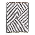 Woven blanket in white with black diagonal line panels meeting at angles and a short fringed edge, laid flat