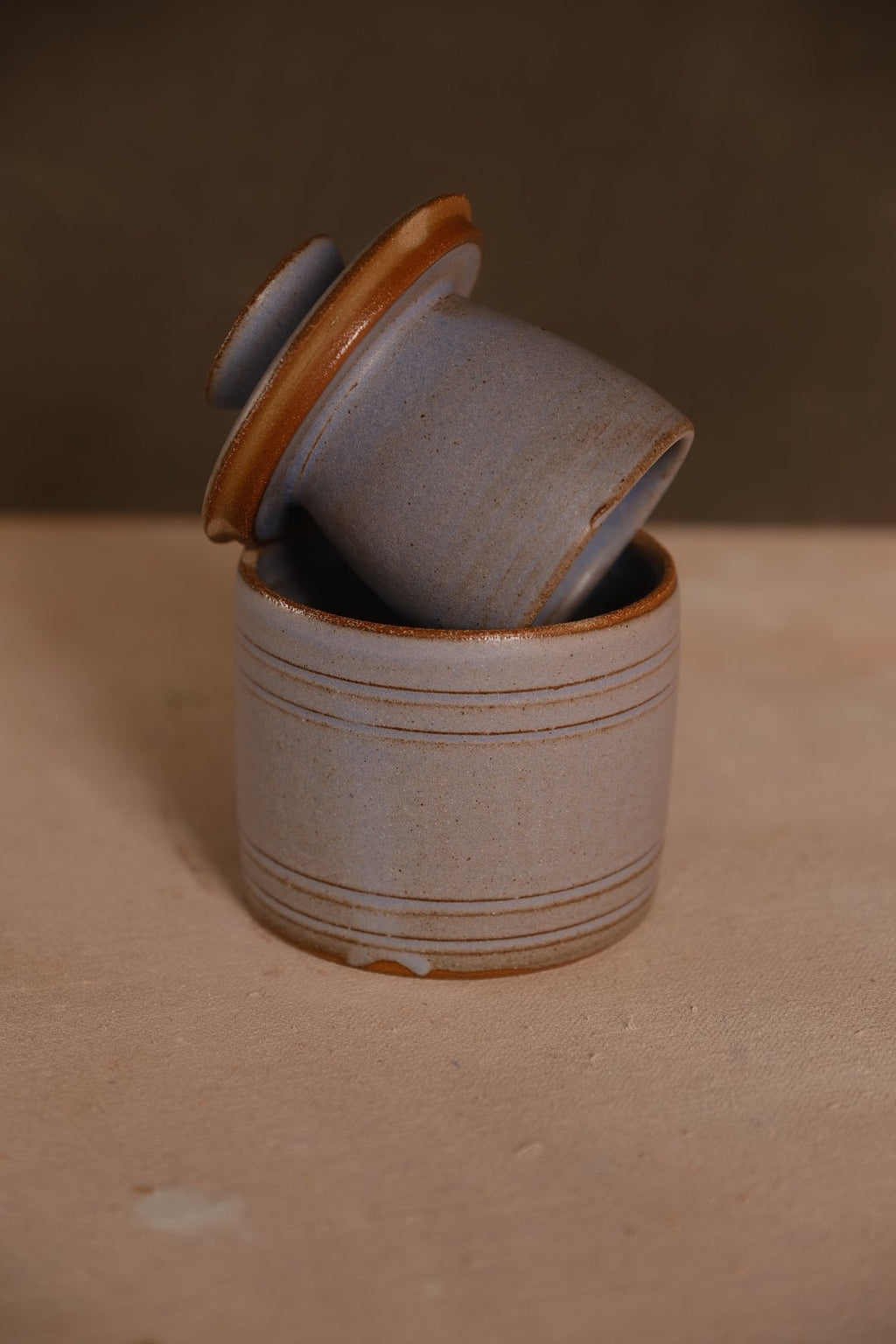 Stoneware French butter keeper in a pale blue-gray glaze with thin rust rings, bell lid tilted in the crock