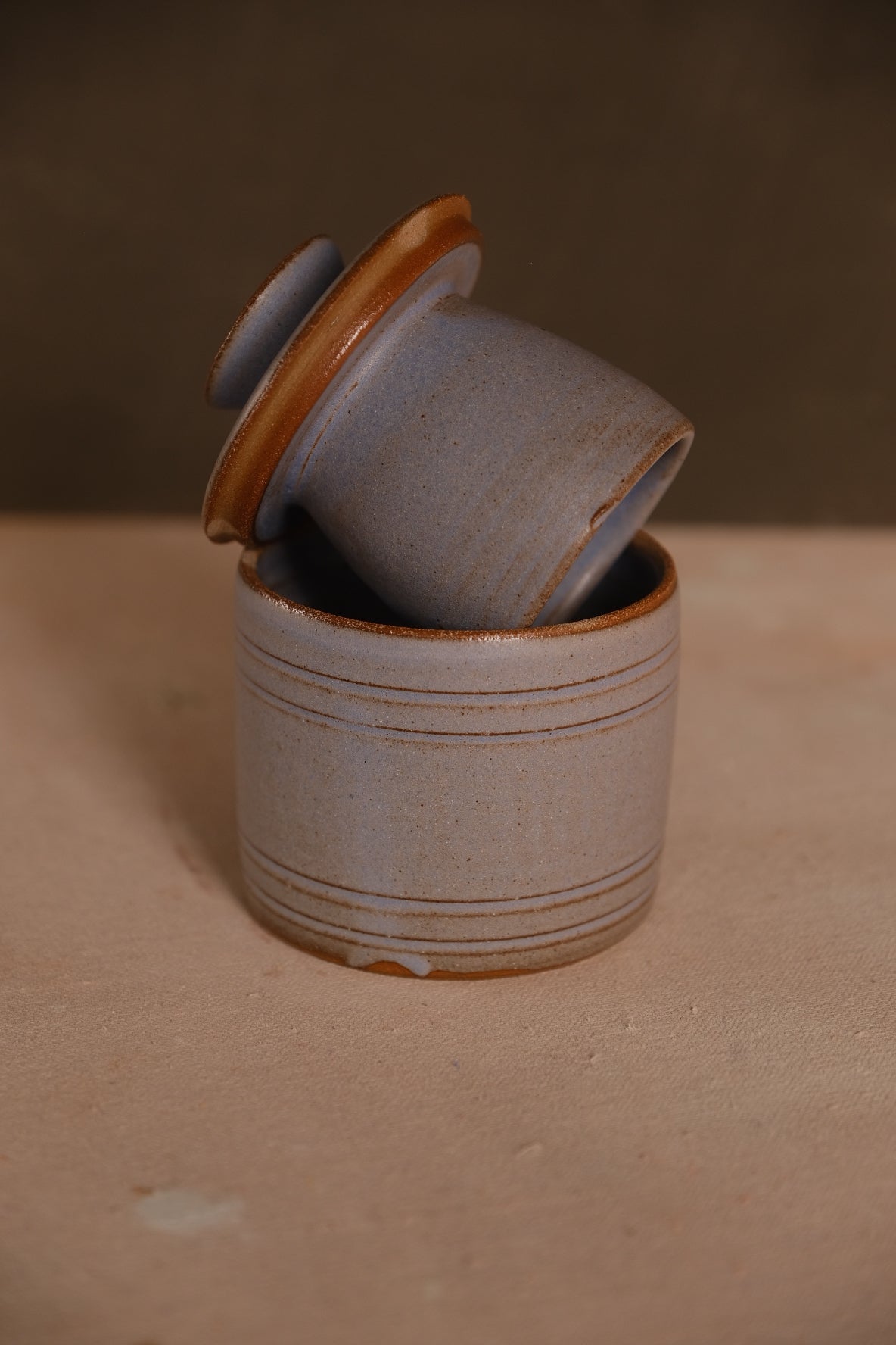 Stoneware French butter keeper in a pale blue-gray glaze with thin rust rings, bell lid tilted in the crock