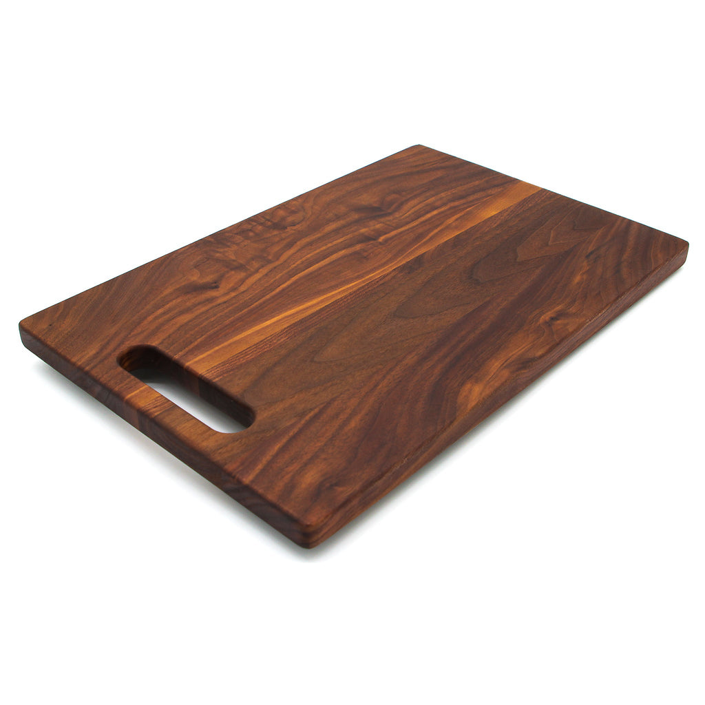 Walnut single handle cutting board, 16 x 10.5 in, lying at an angle on white with the handle toward the front