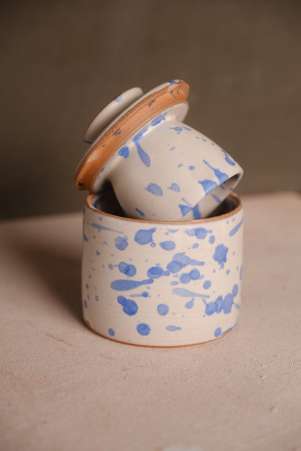 Stoneware French butter keeper in white with cobalt blue splatter, lid tipped to show the butter bell inside