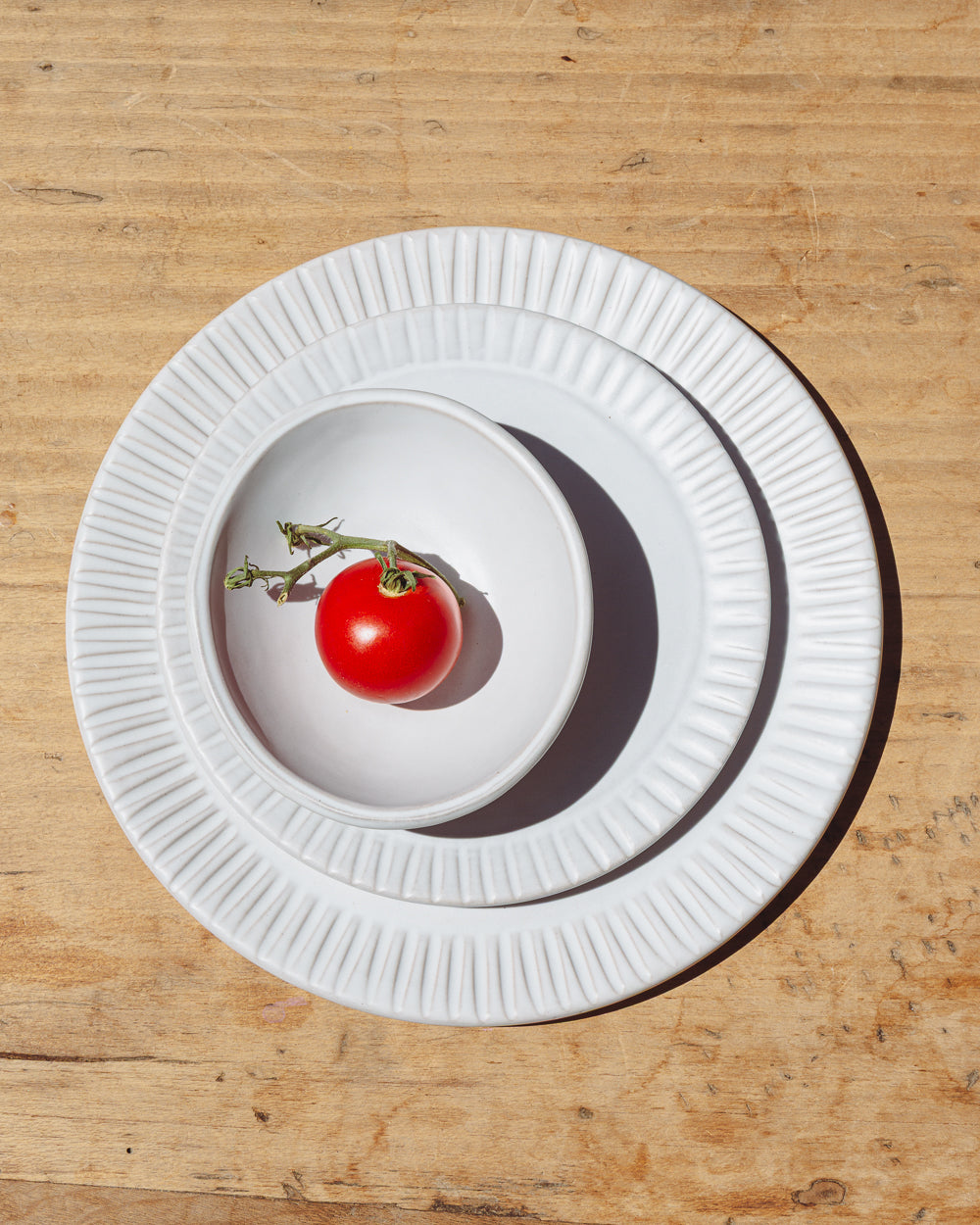 Matte white dinner plate stacked with a salad plate and bowl, a cherry tomato inside, on a wood tabletop