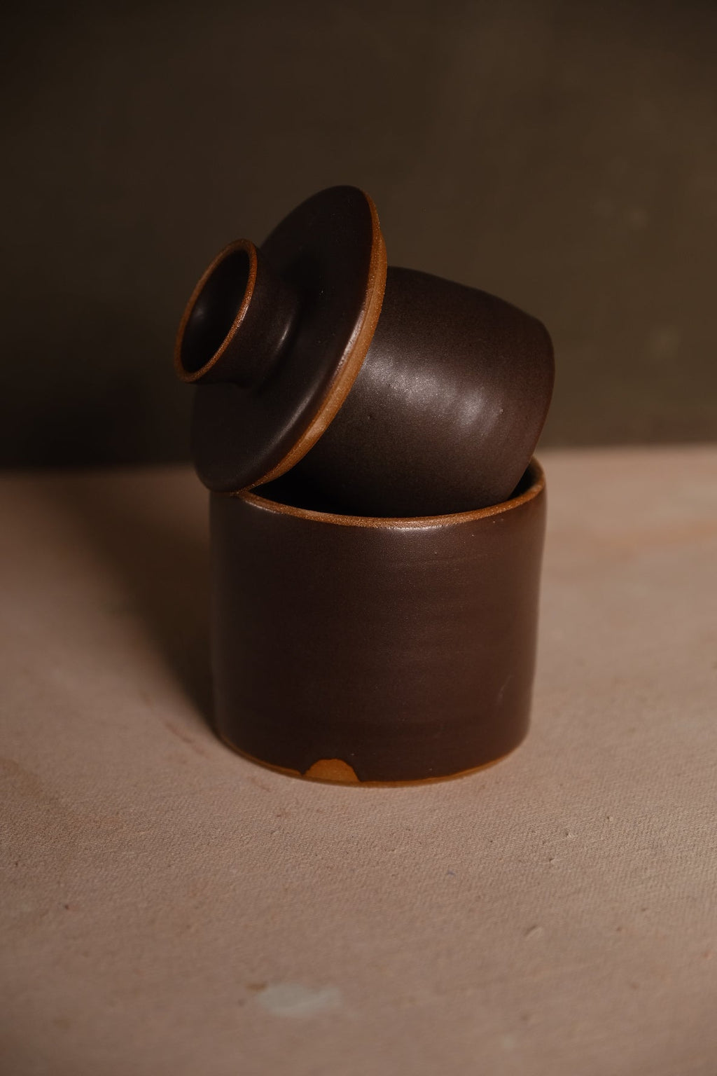Stoneware French butter keeper in a dark espresso brown glaze, bell lid tilted out of the base to show its shape
