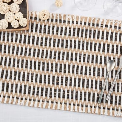 Woven stitch placemat in black, tan and white on a white tablecloth with a spoon, knife and bowl of rattan balls