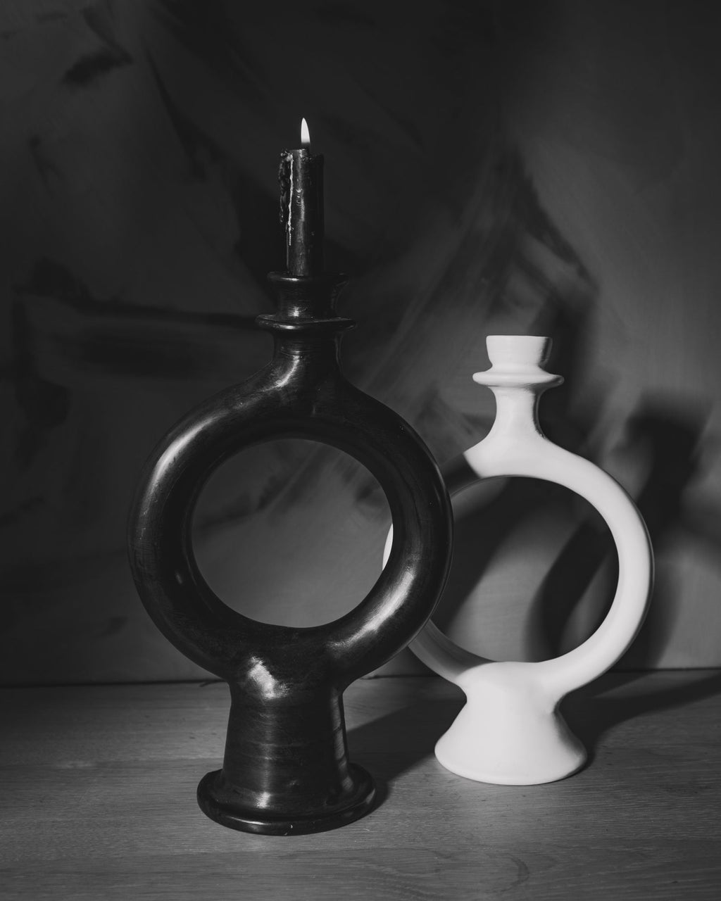 Black and white ring candle holders with tapers on a dark surface in moody gray light