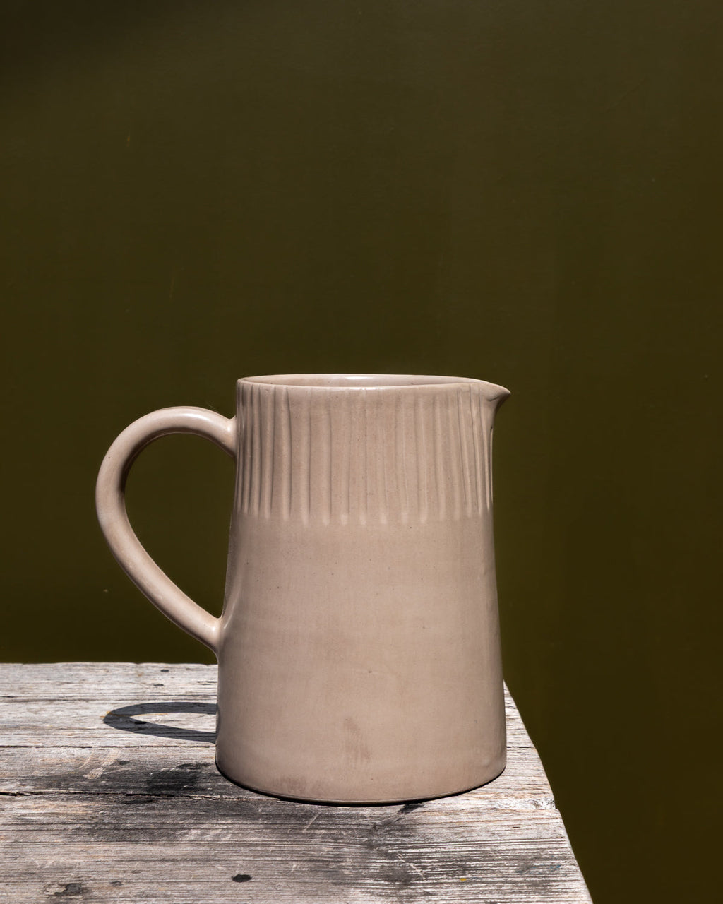 Large carved clay-toned pitcher on a marble ledge in front of a dark olive green wall