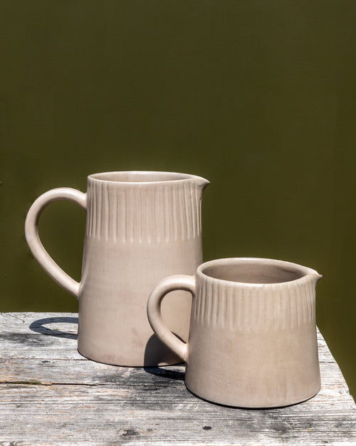 Large and small clay-toned carved ceramic pitchers on a marble counter against a dark olive wall