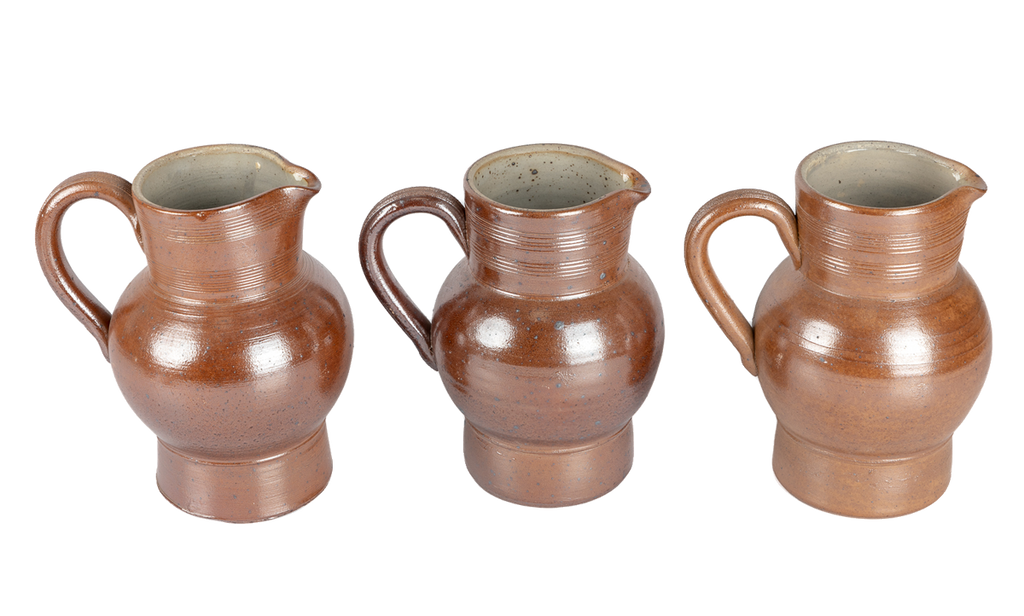 Three vintage salt-glazed French pitchers side by side, each a slightly different shade of toffee brown