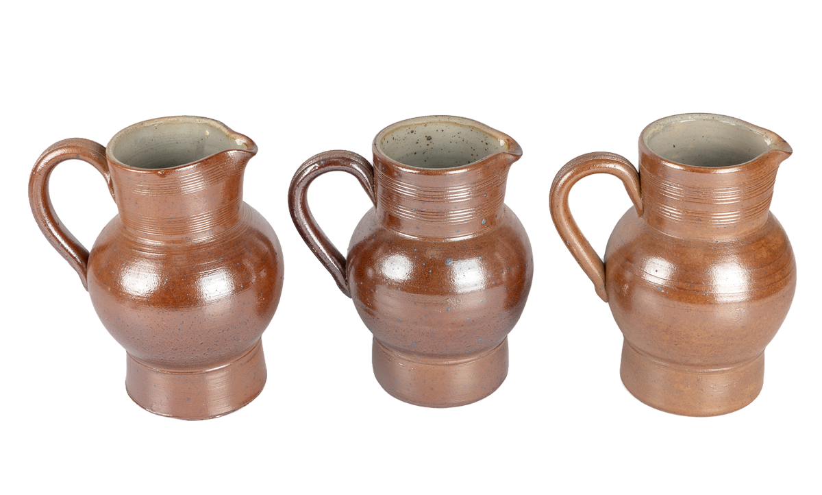 Three vintage salt-glazed French pitchers side by side, each a slightly different shade of toffee brown