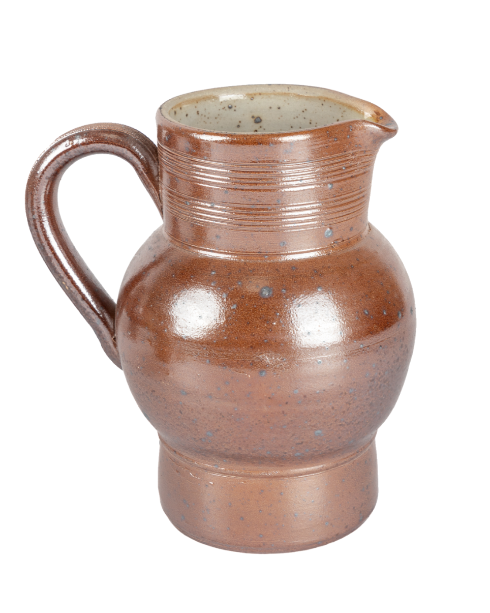 Side view of a vintage brown ceramic pitcher with a looped handle and fine throwing rings against black