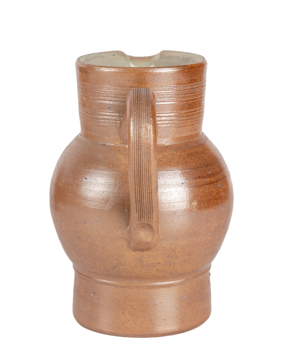 Rear view of a salt-glazed French pitcher showing the handle and footed base against a black background