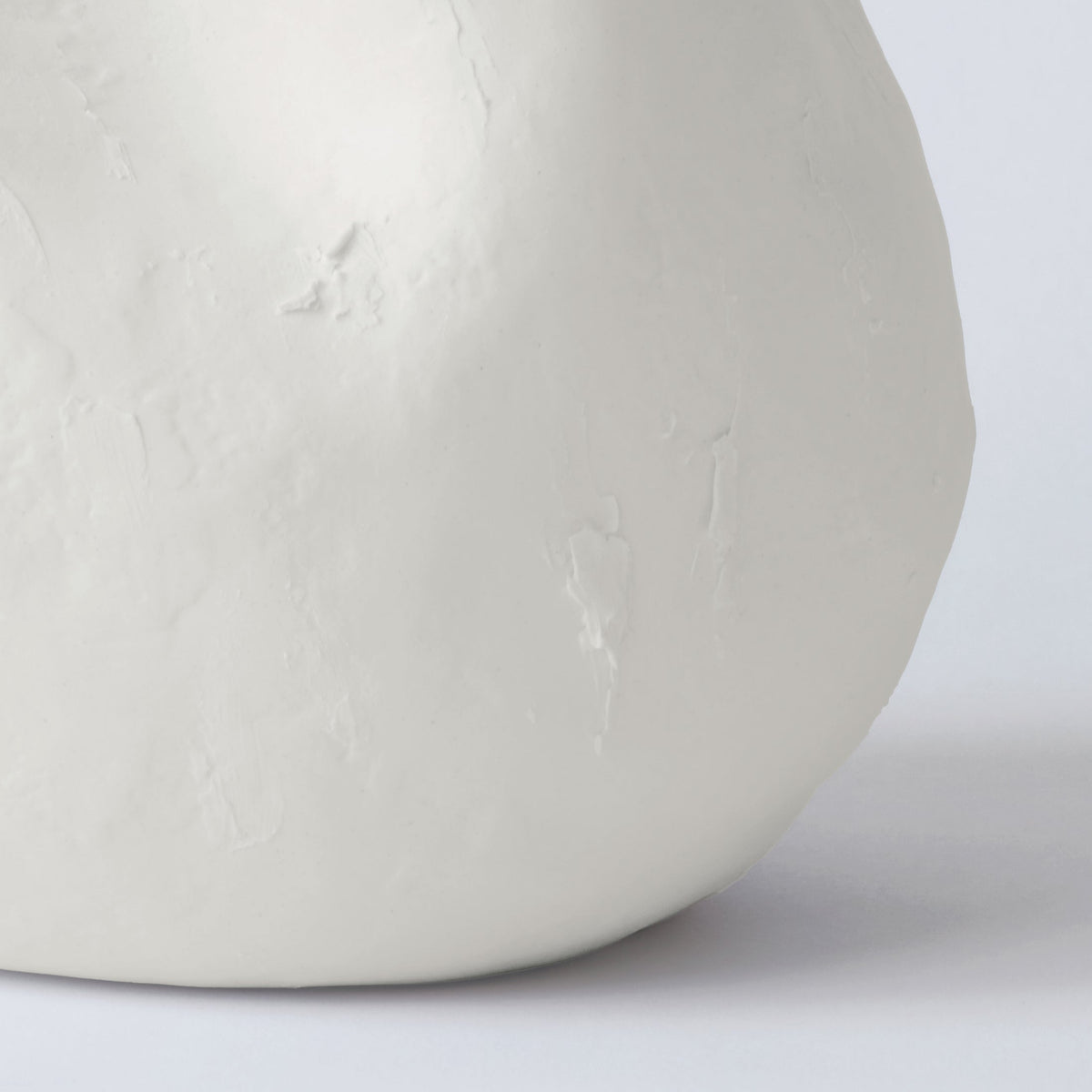 Close detail of the full rounded base of a white sculpted porcelain vase showing its hand-pressed texture