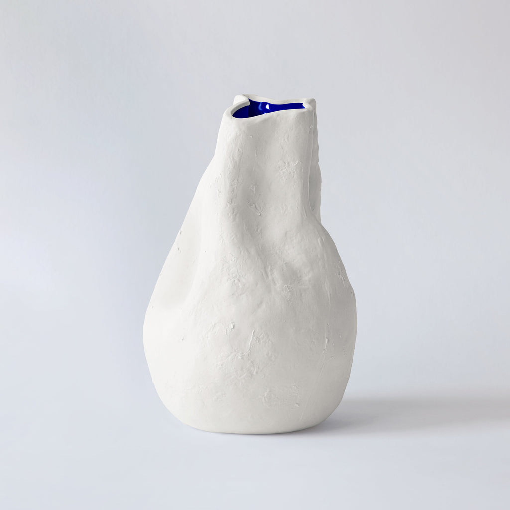 Pear-shaped white porcelain vase turned to show its leaning neck and a glimpse of glossy cobalt inside