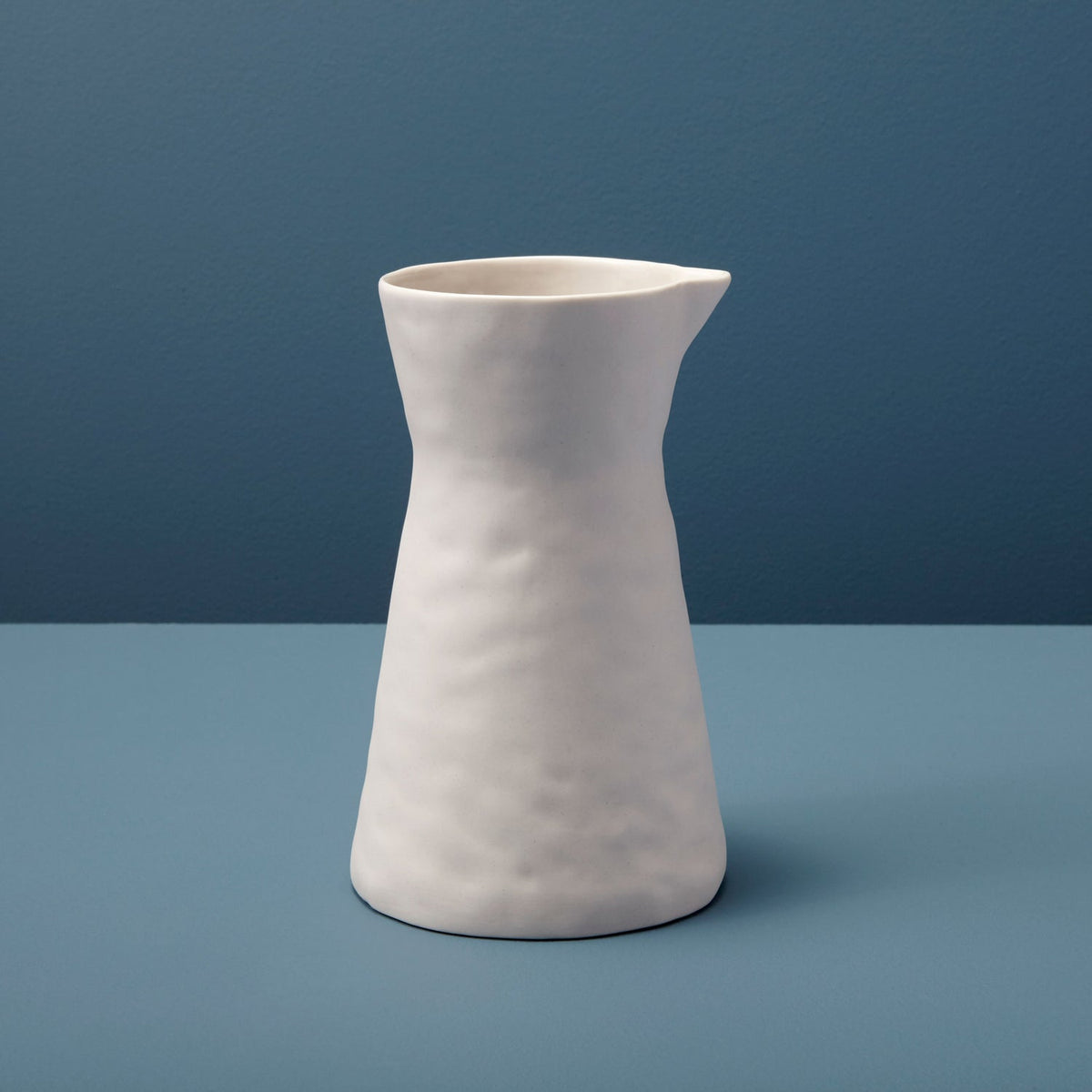 Matte pearl stoneware carafe with a soft rippled surface photographed against a deep slate blue backdrop