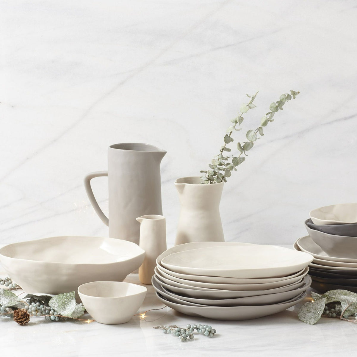 Pearl stoneware carafe among matching plates, bowls and a small jug with eucalyptus on a white marble counter