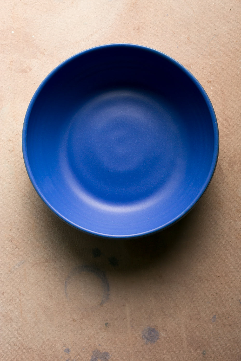 Hand-thrown stoneware serving bowl in a bright cobalt blue glaze seen from above on a pale pink surface