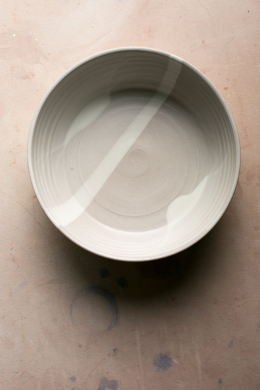 Hand-thrown stoneware serving bowl in a soft cream white glaze seen from above on a pale pink surface