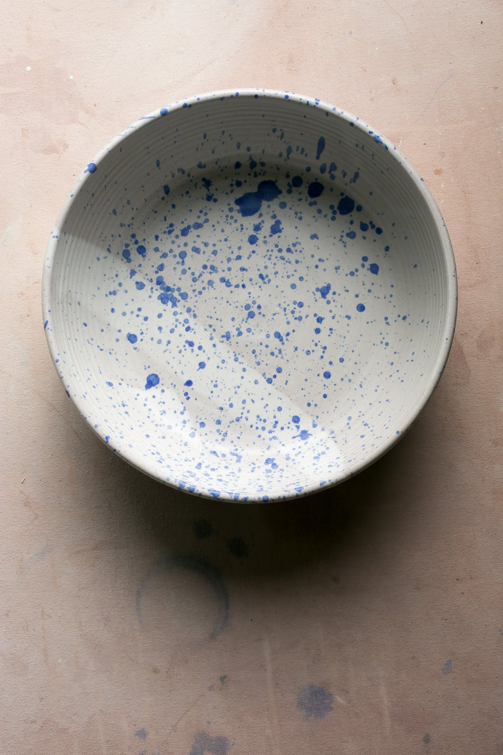 White stoneware serving bowl flecked with small cobalt blue speckles seen from above on a pink surface