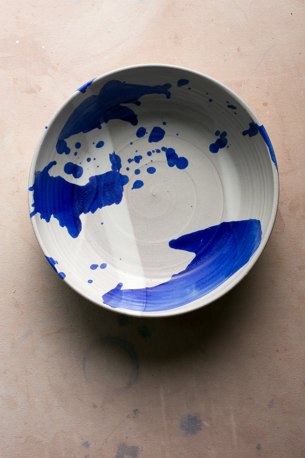 White stoneware serving bowl with bold cobalt blue splashes of glaze seen from above on a pink surface