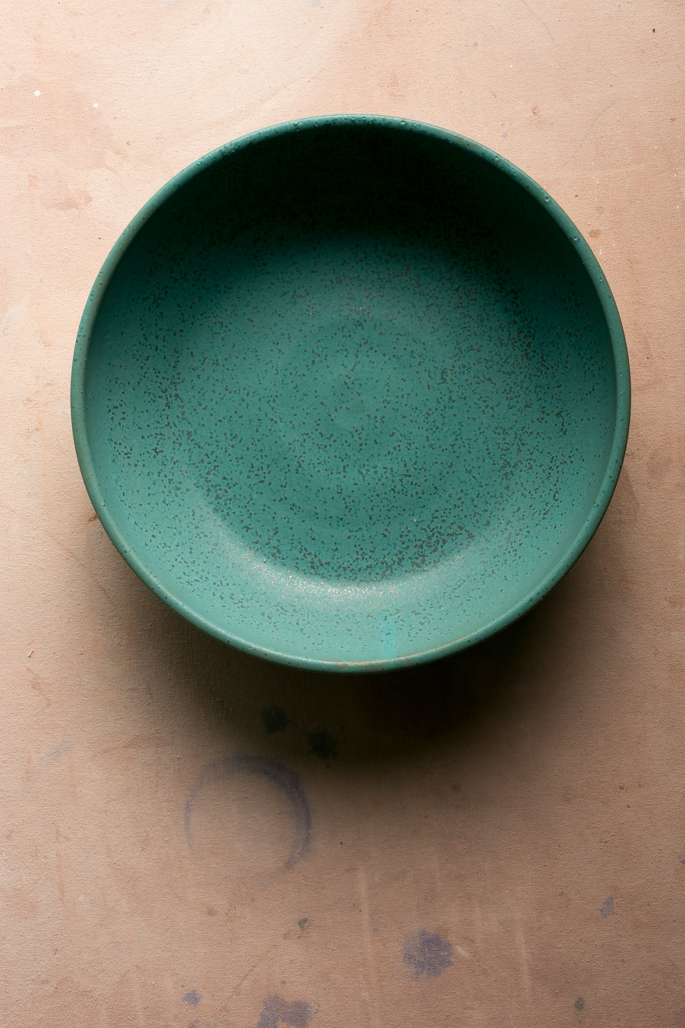 Hand-thrown stoneware serving bowl in a deep green glaze seen from above on a pale pink surface