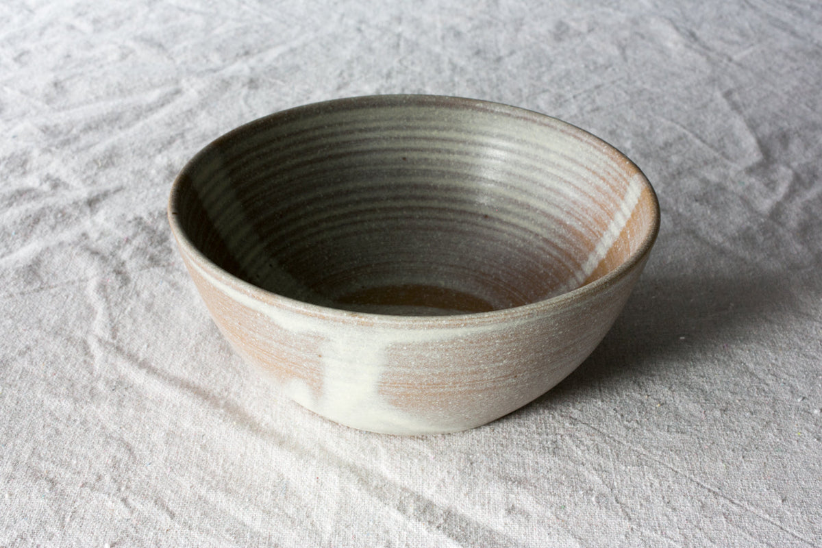 Hand-thrown stoneware soup bowl in a pale oat glaze with grey throwing rings sitting on a white linen cloth