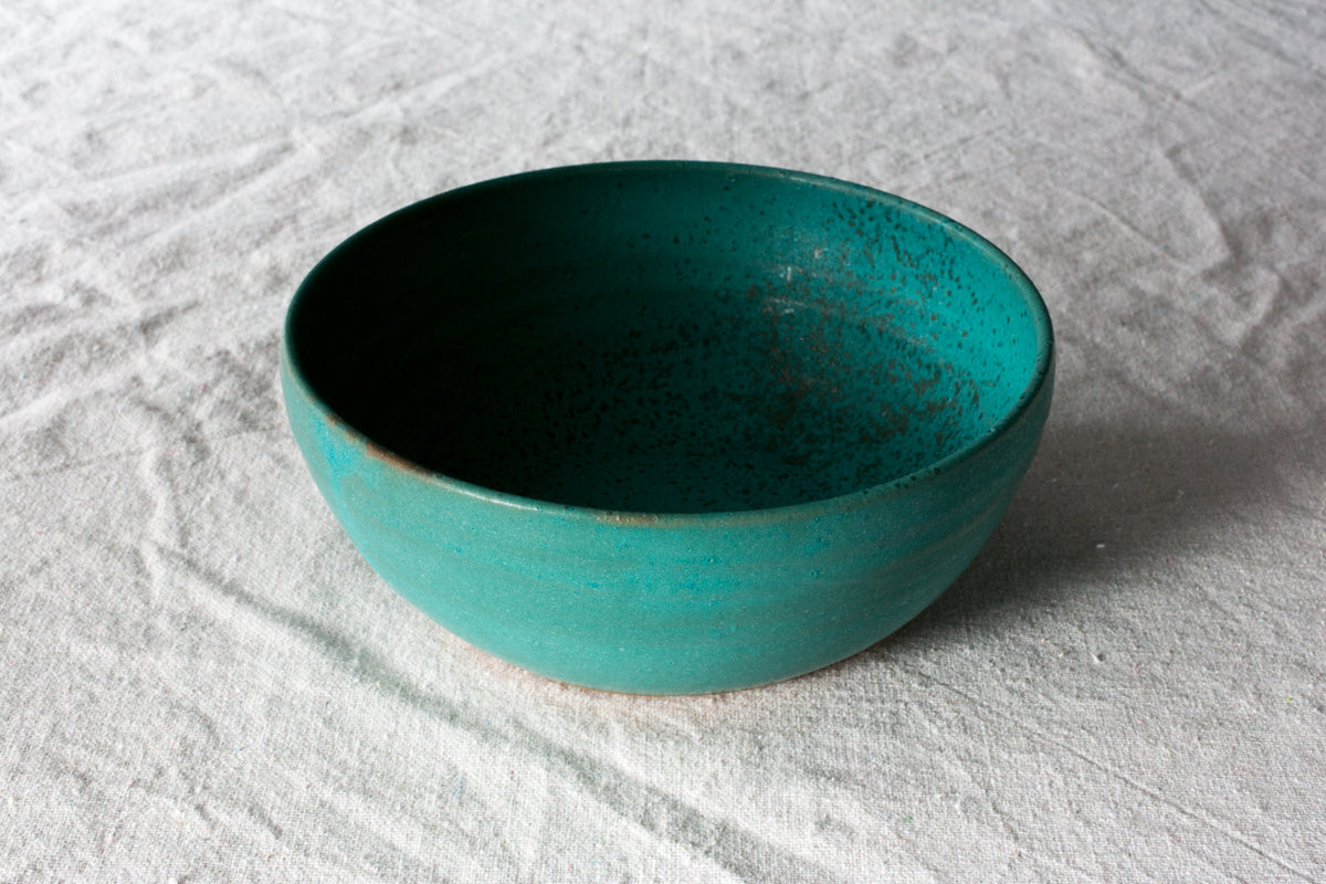 Hand-thrown stoneware soup bowl in a speckled turquoise glaze with a dark interior on a white linen cloth
