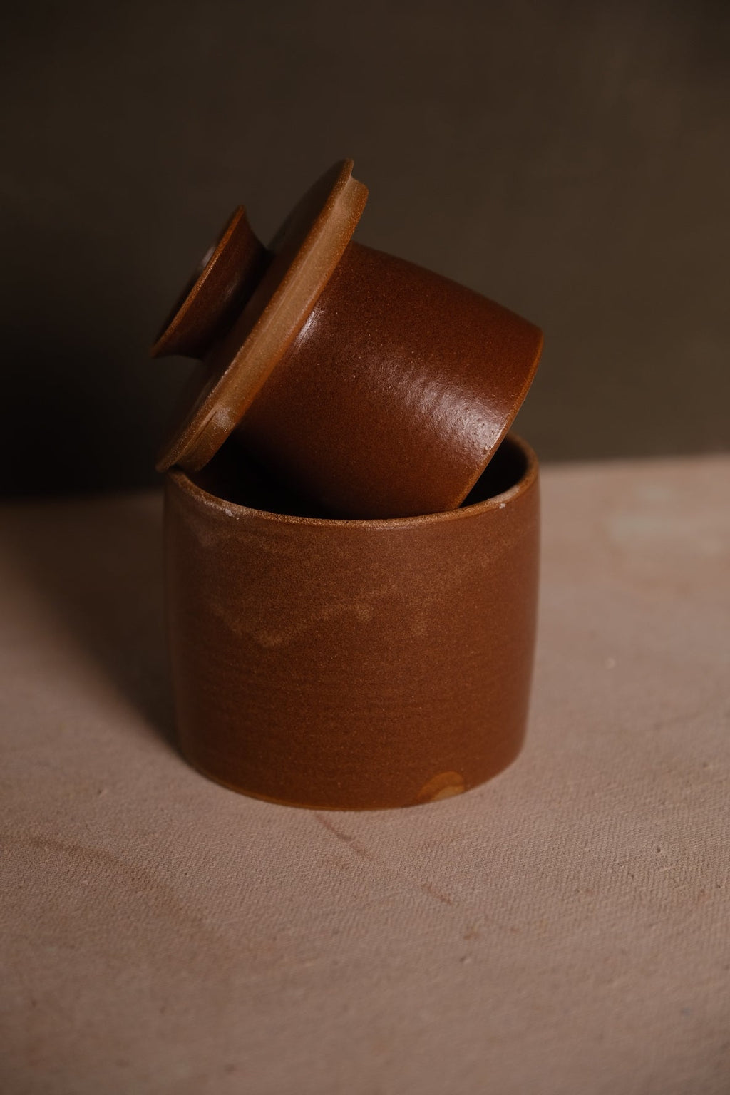 Stoneware French butter keeper in a red-brown rust glaze, bell lid leaning out of the round crock base