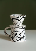 Splatter glazed stoneware pour-over dripper stacked on a matching pitcher against a dark olive green wall