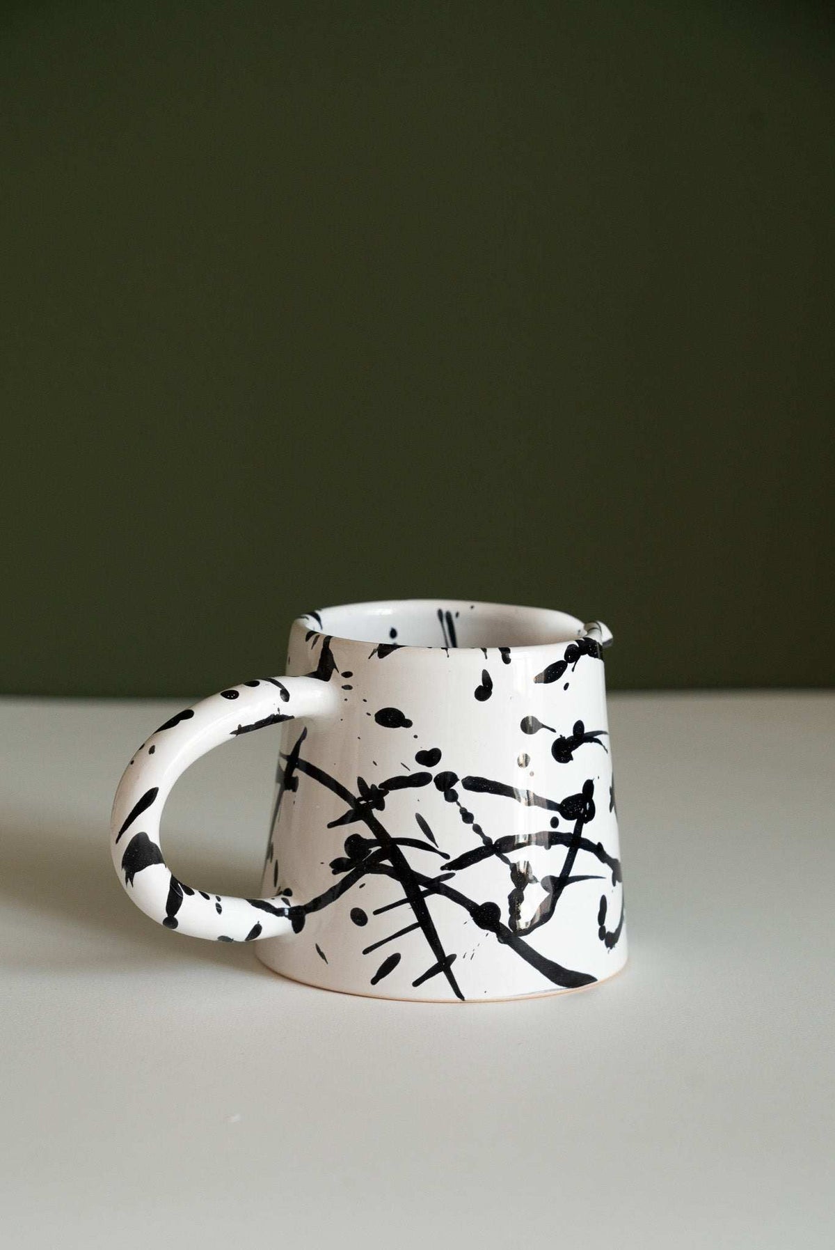Splatter glazed stoneware pitcher shown on its own with its rounded handle to the left