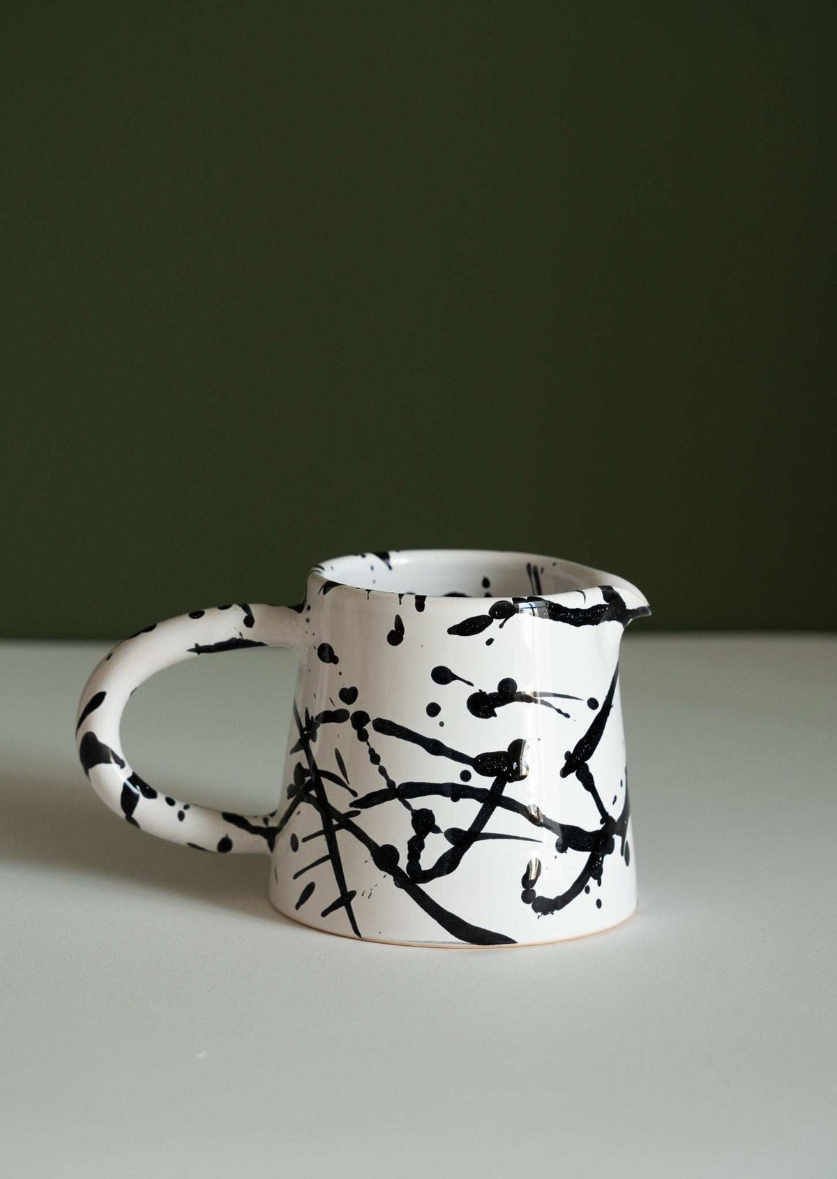 Black and white splatter stoneware pitcher with a wide handle shown on its own on a white surface