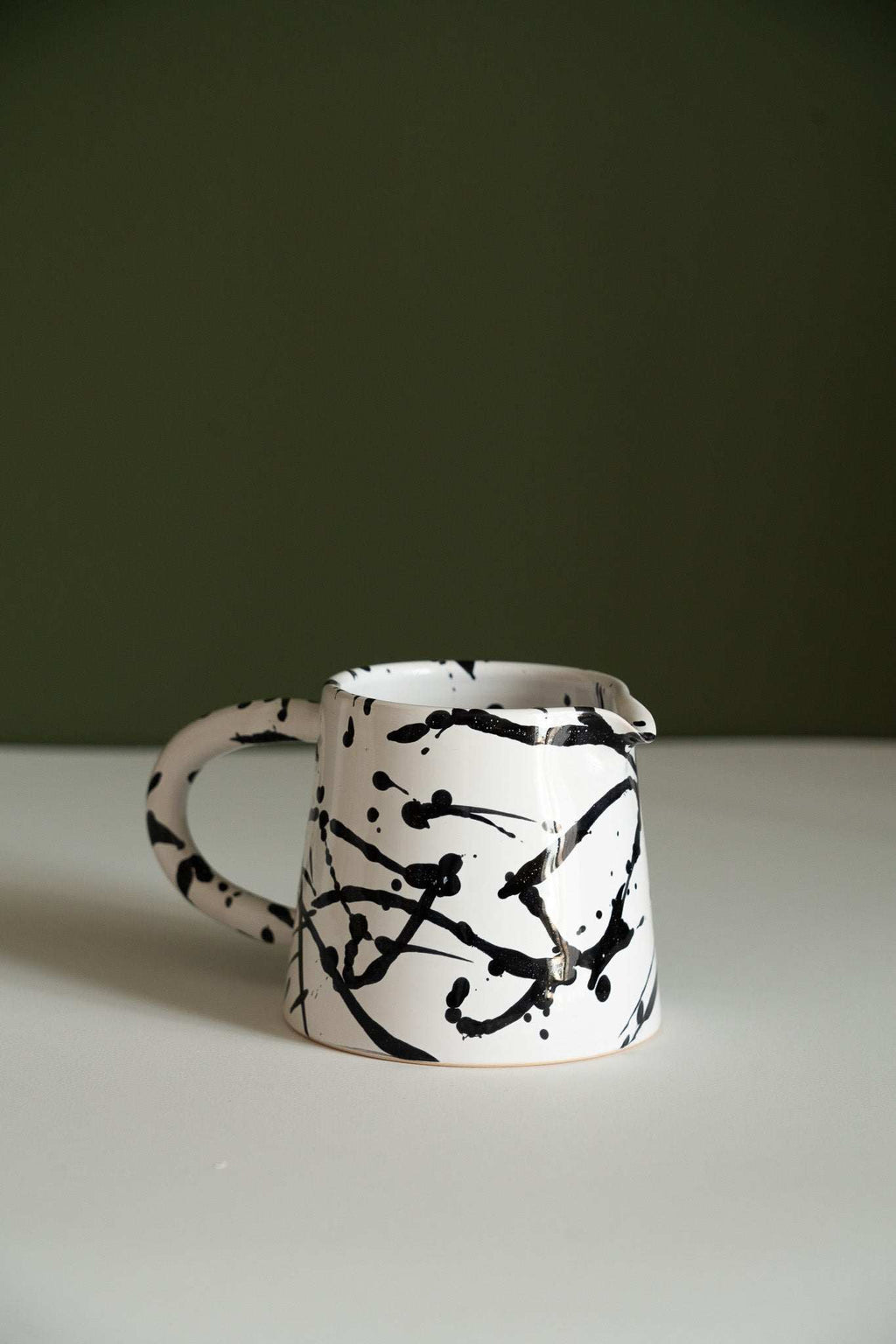 Fine black speckle stoneware pitcher shown on its own against a dark olive green background