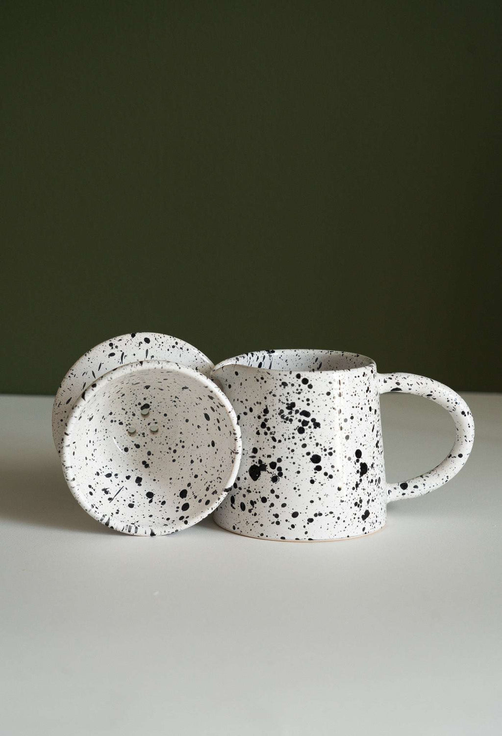 Speckled cone dripper tipped forward beside its pitcher to show the inside and filter hole
