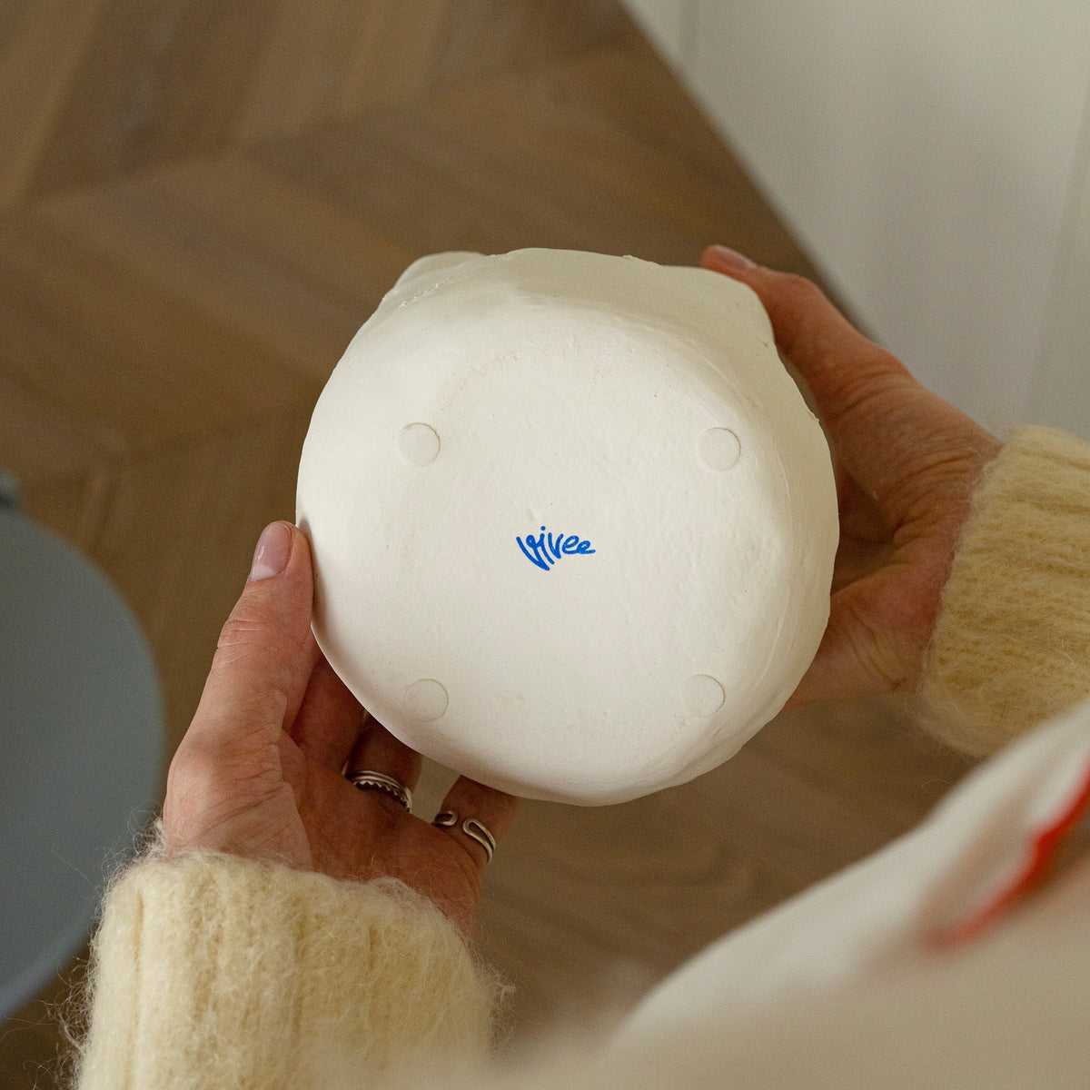 Hands turning over a tall white porcelain vase to show its rounded base and small blue maker's mark