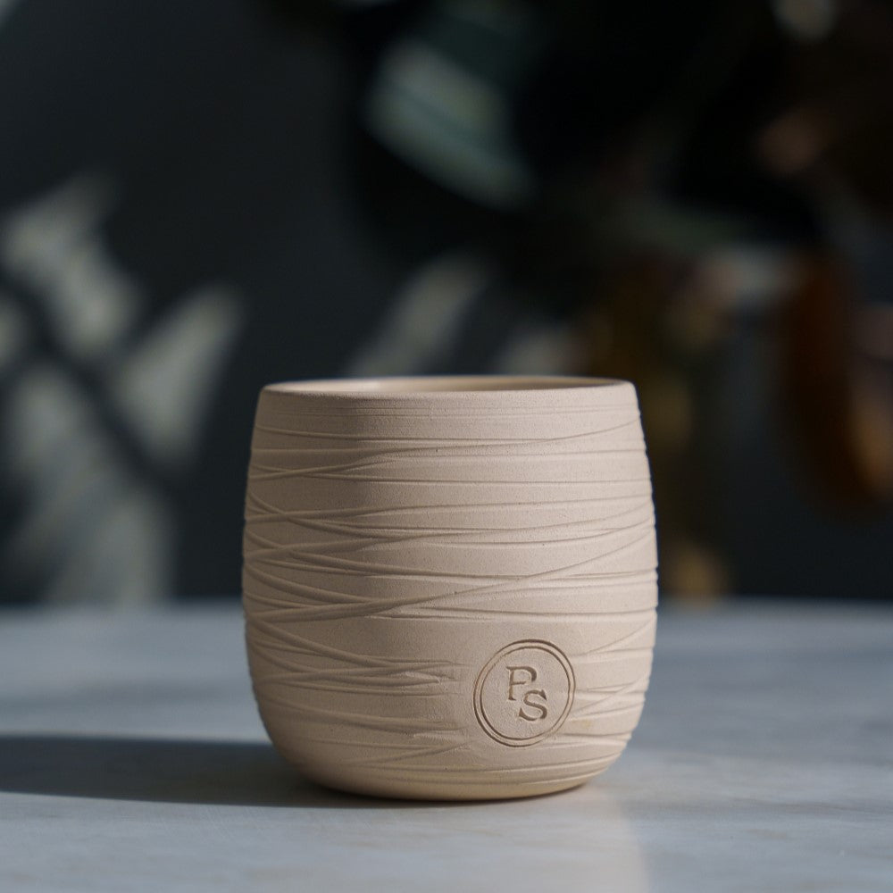 Sandalwood candle in a carved sand-colored clay vessel with an embossed seal on a stone tabletop
