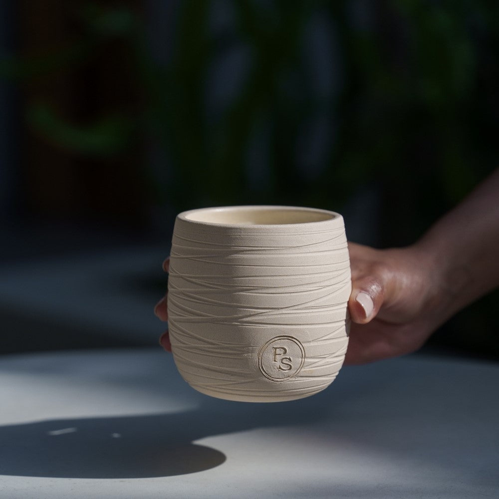 Hand placing the textured clay neroli candle down on a gray stone table in dappled afternoon shade