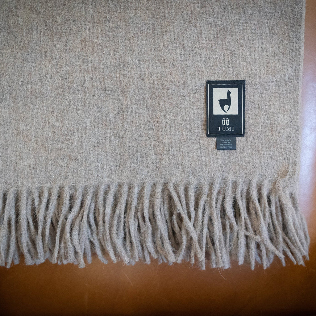 Tan alpaca wool blend throw with long fringe draped over the back of a tan leather armchair