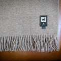 Tan alpaca wool blend throw with long fringe draped over the back of a tan leather armchair