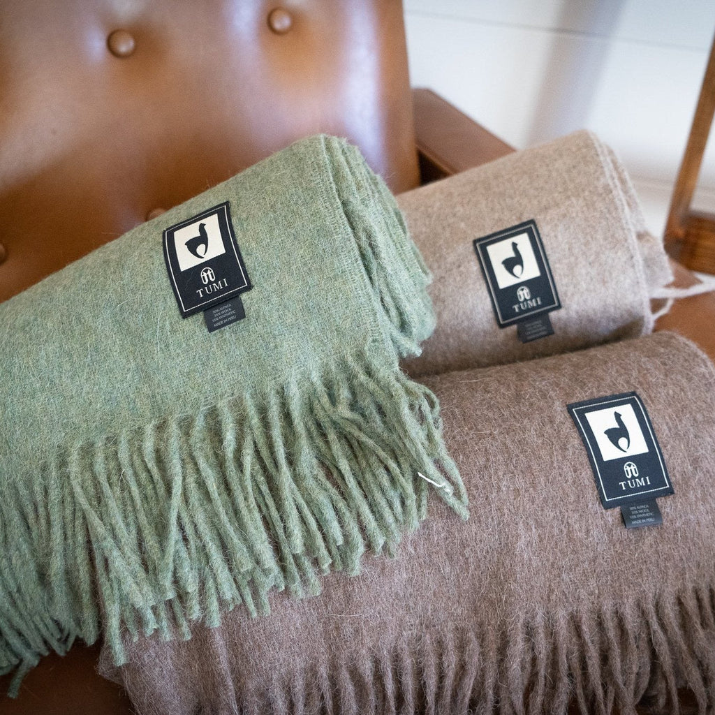 Rolled alpaca wool blend throws in green, tan and brown stacked on a tufted tan leather chair
