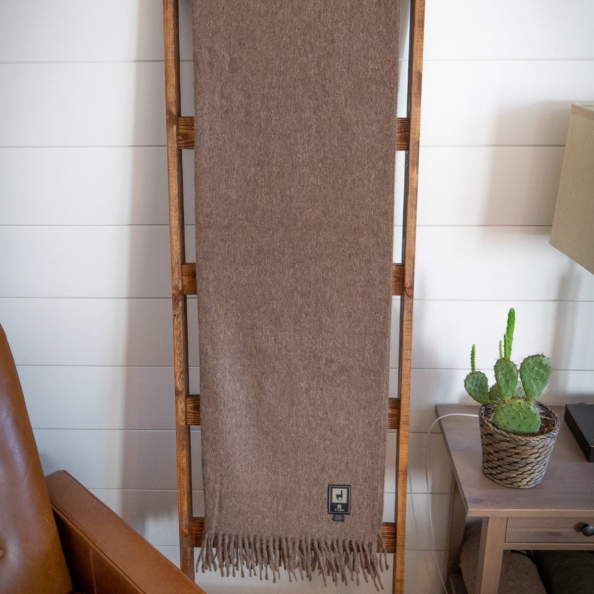 Brown alpaca wool blend throw hanging full length on a wooden ladder beside a small potted cactus