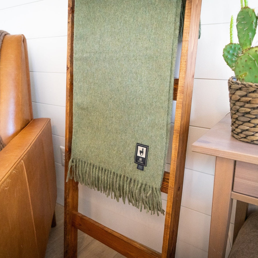 Green alpaca wool blend throw on a wooden blanket ladder with a brown throw on a nearby leather chair